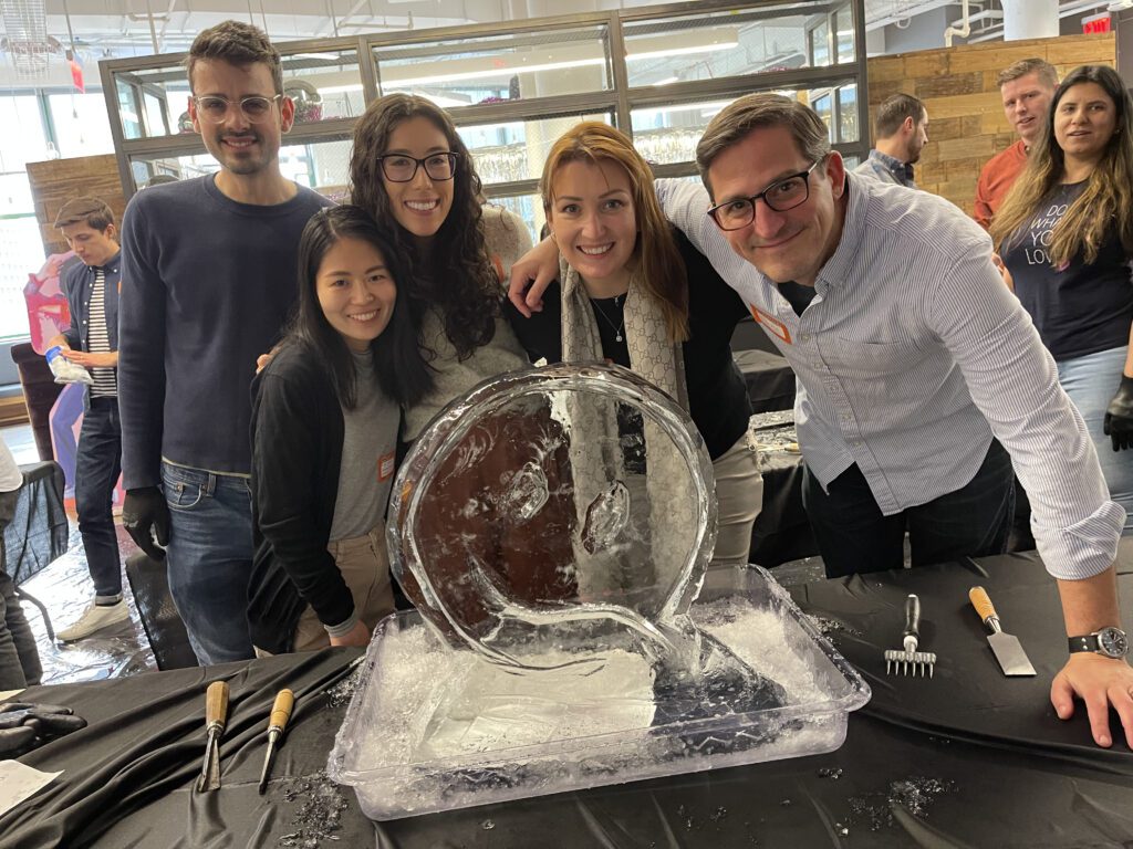 A team poses proudly beside their nearly completed ice sculpture during a Team building Ice Sculpting event, demonstrating collaboration and creativity.