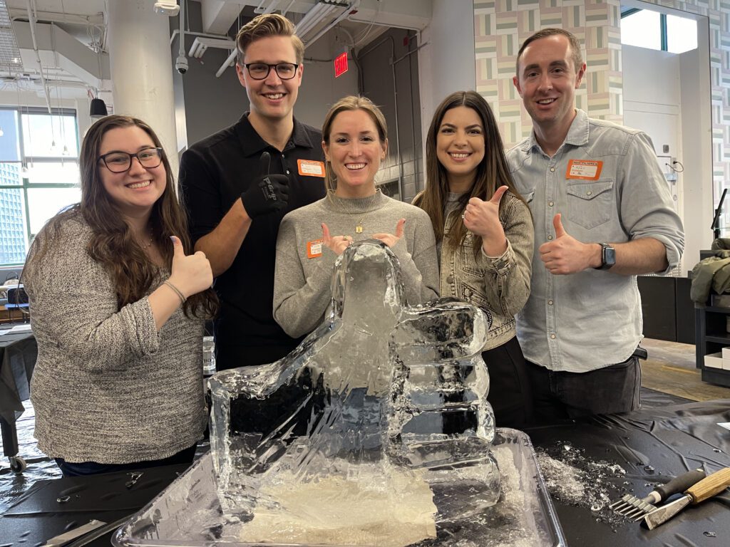 A team proudly poses with their completed ice sculpture during a Team building Ice Sculpting event, showcasing their creativity and teamwork in crafting the intricate design.