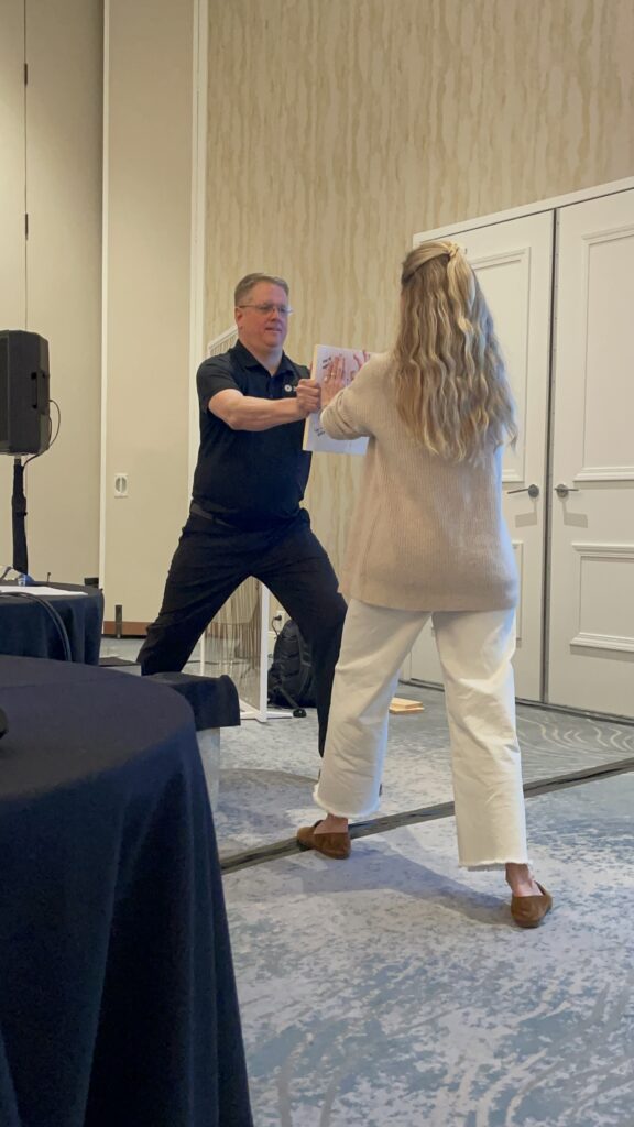 A facilitator guides a participant through a board-breaking exercise during a transformative team building event focused on overcoming barriers.