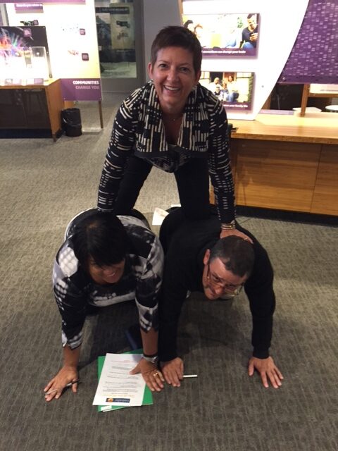 Team members forming a human pyramid during a museum scavenger hunt. This activity encourages teamwork, collaboration, and creative problem-solving while engaging with interactive exhibits.