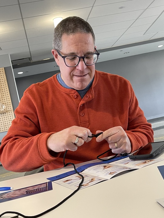 Man focused on tying a paracord during the Paracord Bracelet Making activity at a corporate team building event 'Donation Station'.