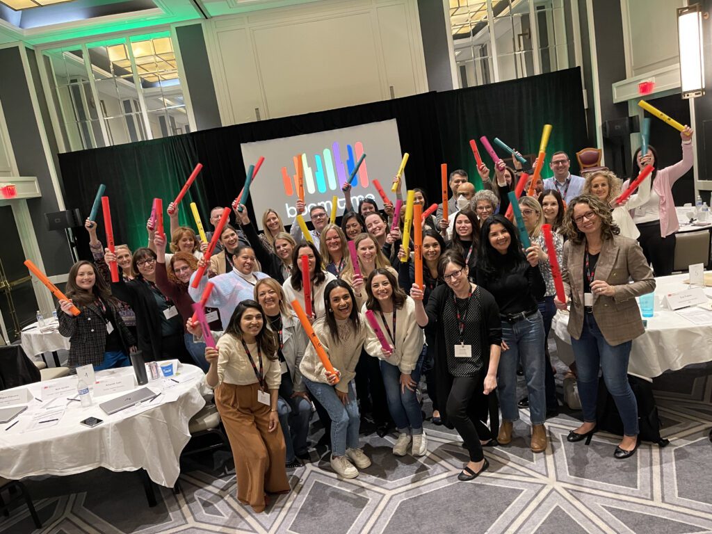 A group of participants at a Boom Time team building event hold colorful Boomwhackers above their heads, smiling and posing together.