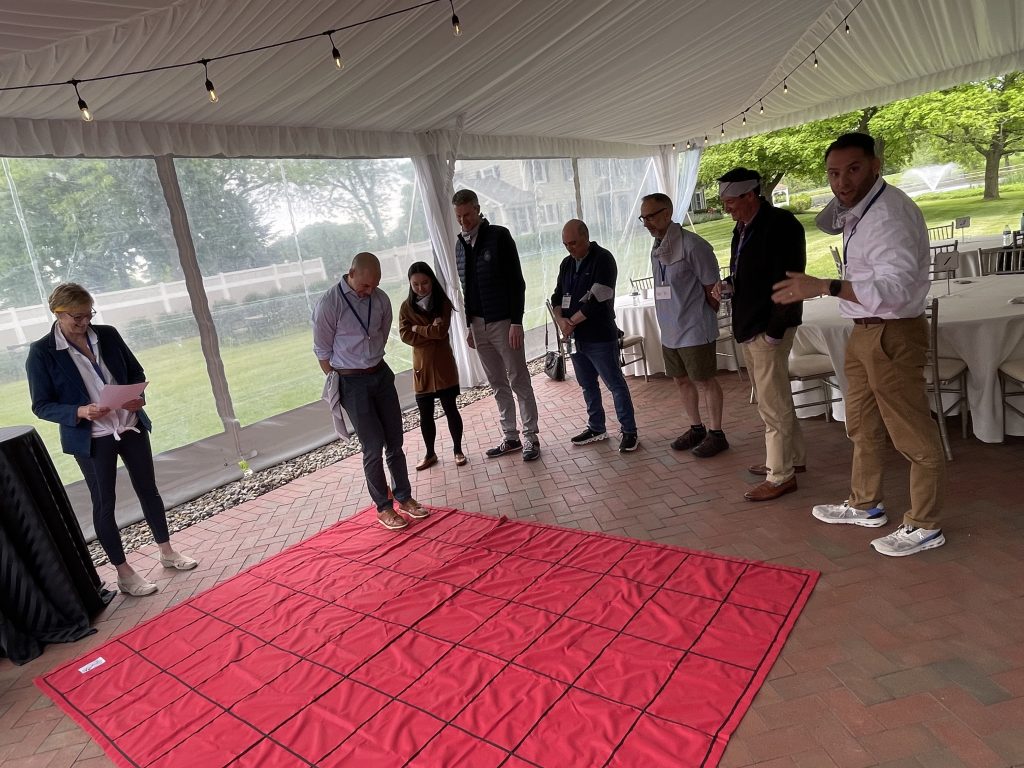 Participants in the Integrity team building event preparing to tackle a challenge on a large red grid, guided by an instructor.