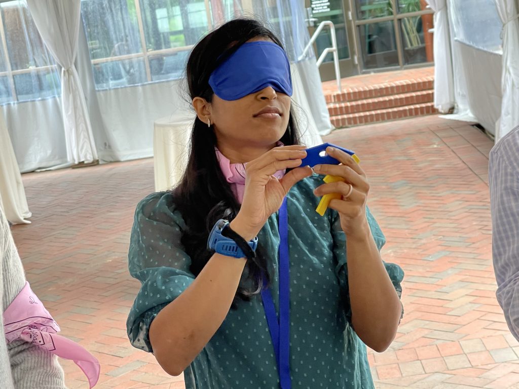 A participant in the Integrity team building event, blindfolded and carefully handling a challenge item, demonstrating focus and teamwork.