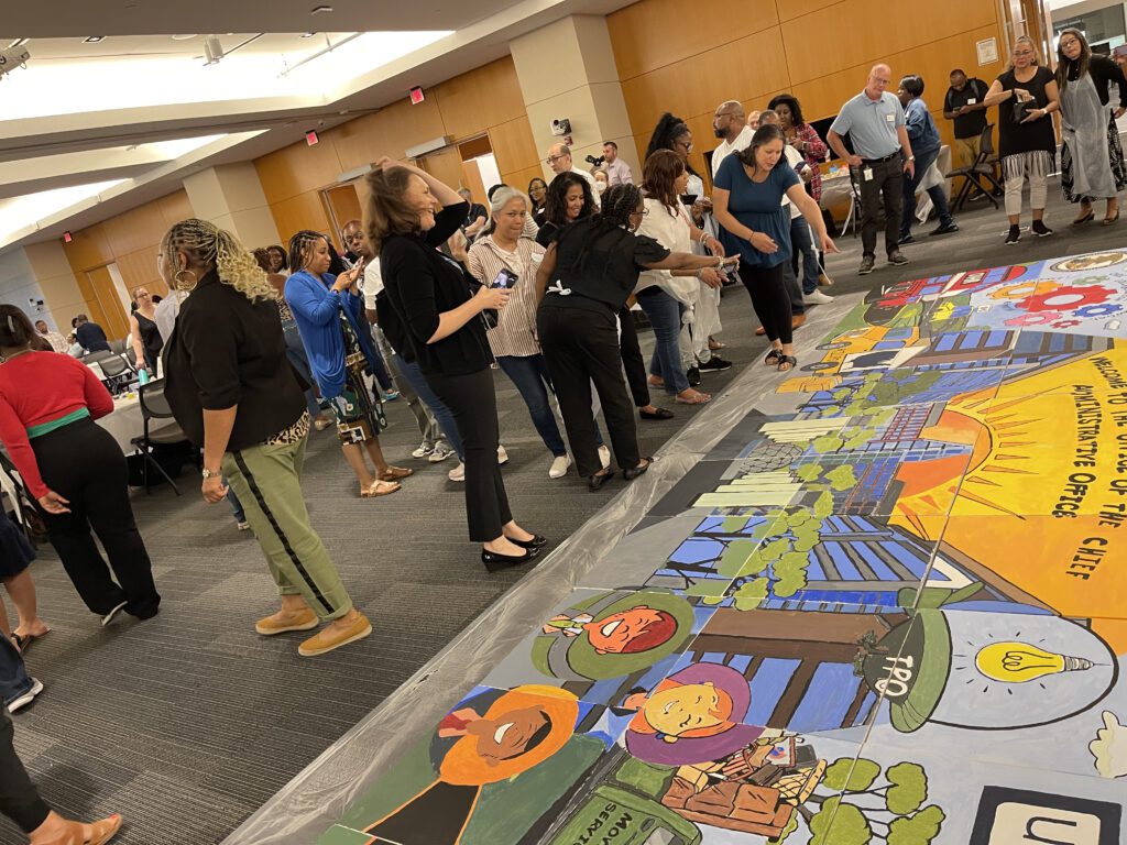 Participants gather to assemble their completed canvases into a large mural during The Big Picture team building event, showcasing their collaborative artwork and teamwork efforts.