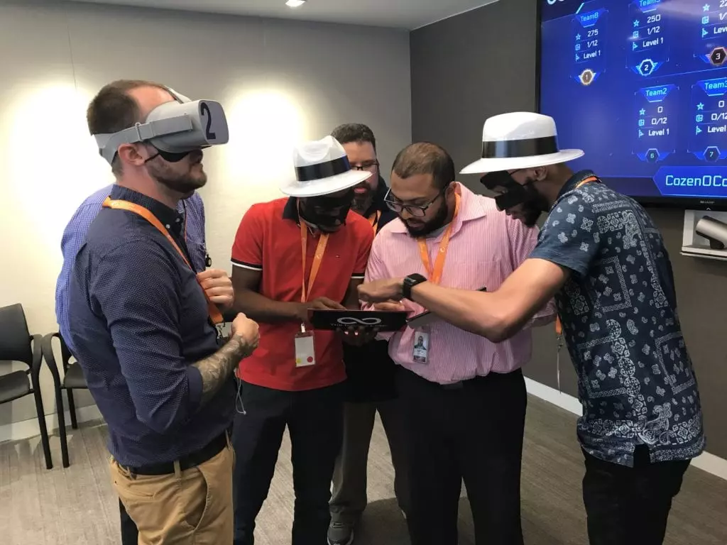 A team of participants in The Infinite Loop team building event collaborates, with some wearing VR headsets and others observing, working together to solve a virtual challenge.