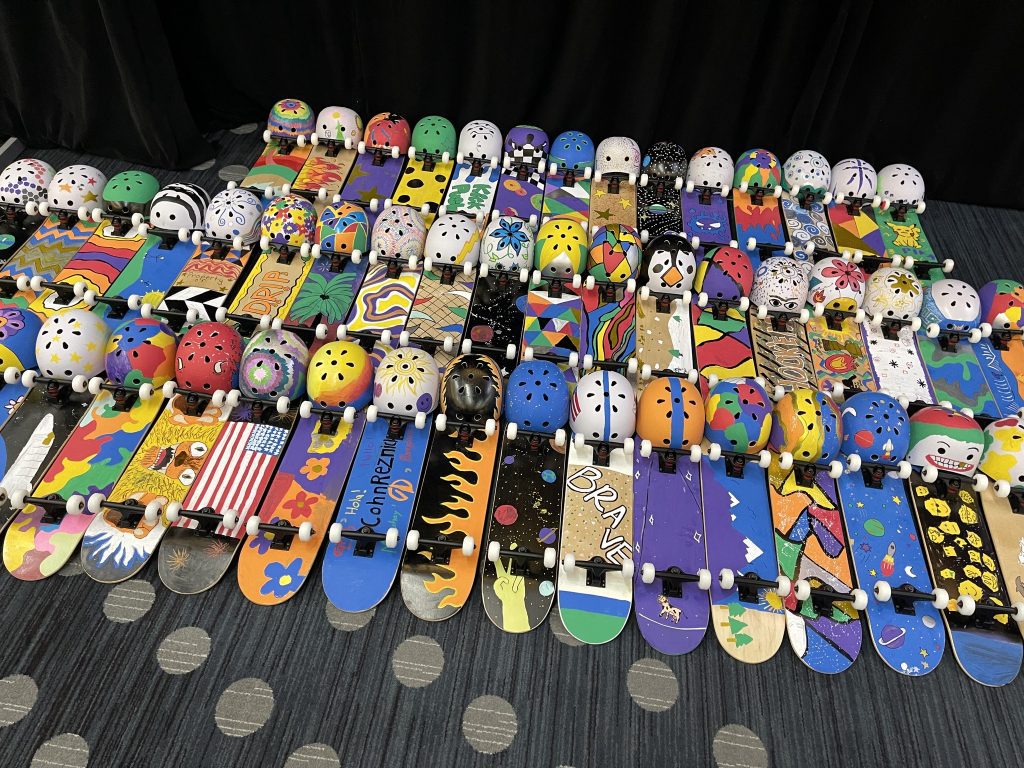 A vibrant display of decorated skateboards and helmets created during the Just Roll With It team building event, showcasing the creativity and teamwork of participants.