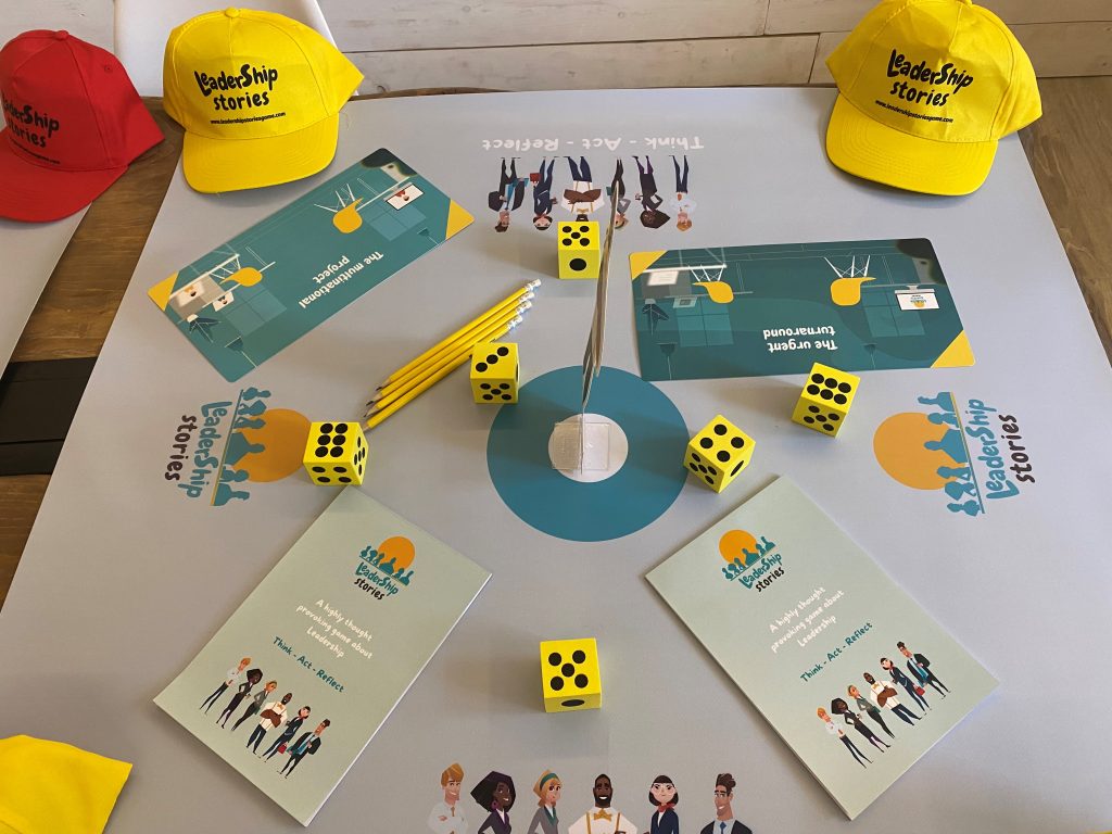 Table setup for the Leadership Stories game, featuring game materials like yellow dice, pencils, booklets, and colorful hats, designed for an interactive leadership team building experience.