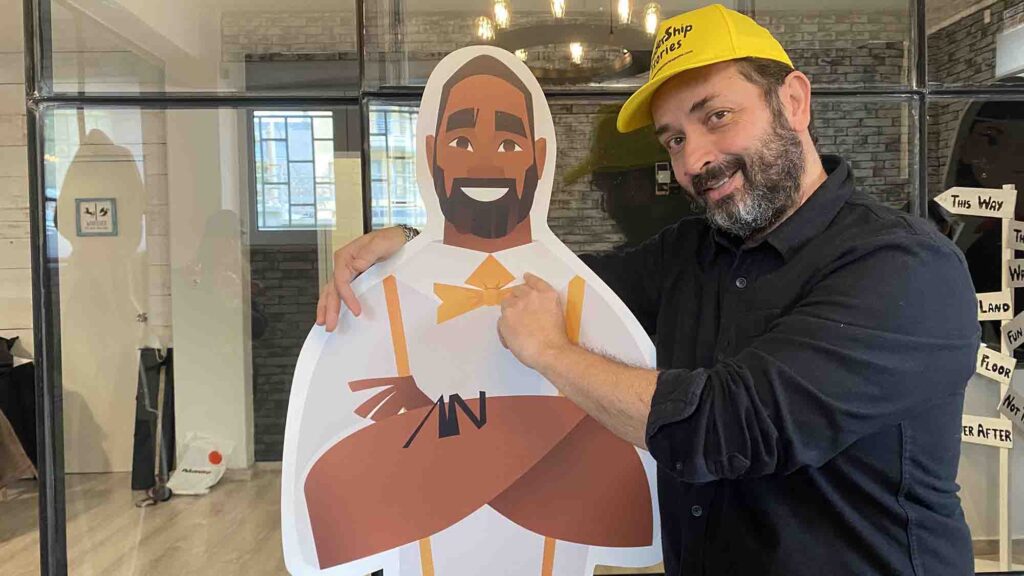 A team member posing with their Leadership Stories game character, smiling and pointing at the cutout.