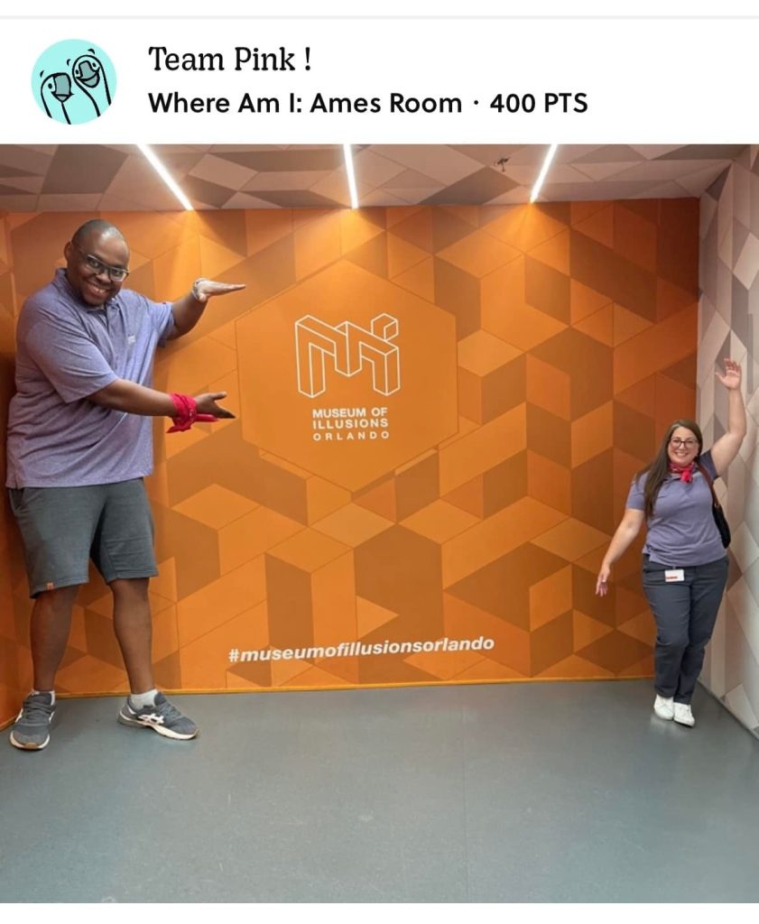 Team Pink posing in the Museum of Illusions' Ames Room during a scavenger hunt. The optical illusion creates a fun challenge, enhancing teamwork and creativity as they engage in the interactive exhibit.