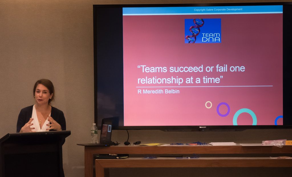 A facilitator leading a Team DNA session with a presentation slide on the screen that reads: 'Teams succeed or fail one relationship at a time' - R Meredith Belbin.