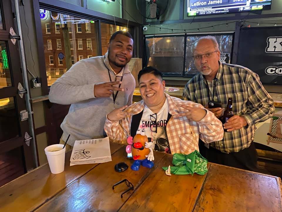 Team enjoying their Pub Crawl Scavenger Hunt, posing with playful props at a local bar, showcasing teamwork and camaraderie during the fun-filled event.