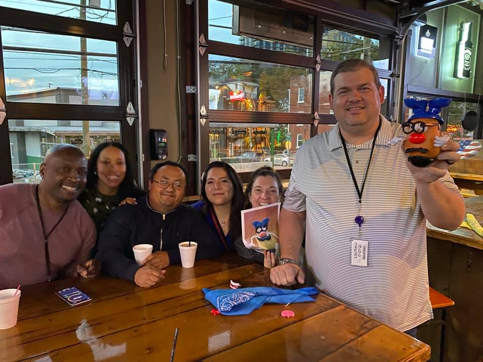 A cheerful group of colleagues enjoying the Pub Crawl Scavenger Hunt, proudly showing off their creative achievements as part of the fun and camaraderie building event.