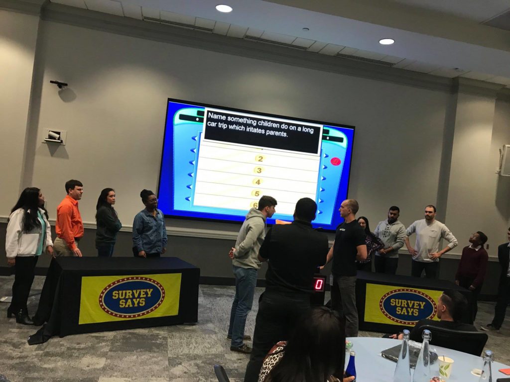 Two teams of participants facing each other and preparing to answer a question displayed on a large screen during the Survey Says team building activity.