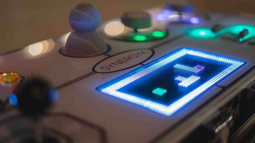 Close-up of the illuminated Team Synergy retro gaming console showcasing bright LED displays, joysticks, and sliders for a team building challenge.