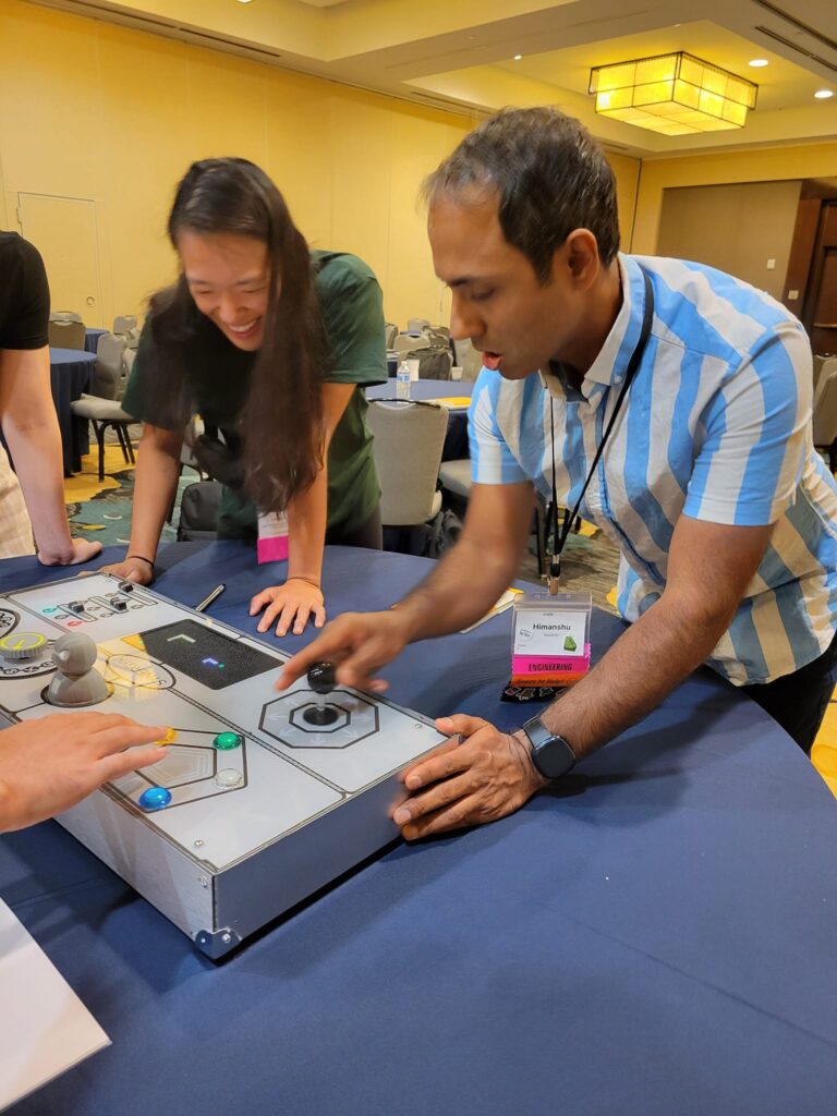 Team member enthusiastically interacting with the Team Synergy console while teammates look on and laugh during a fun team building challenge.