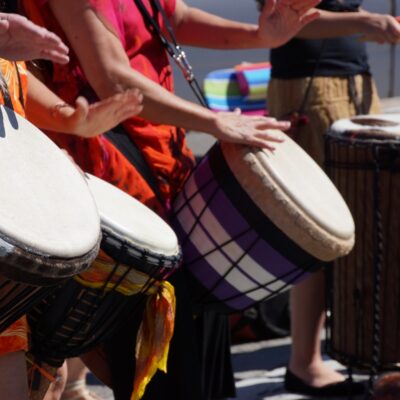 Participants in the Drumming Up A Team event play percussion instruments, collaborating to create a unified rhythm and building team spirit through music and engagement.