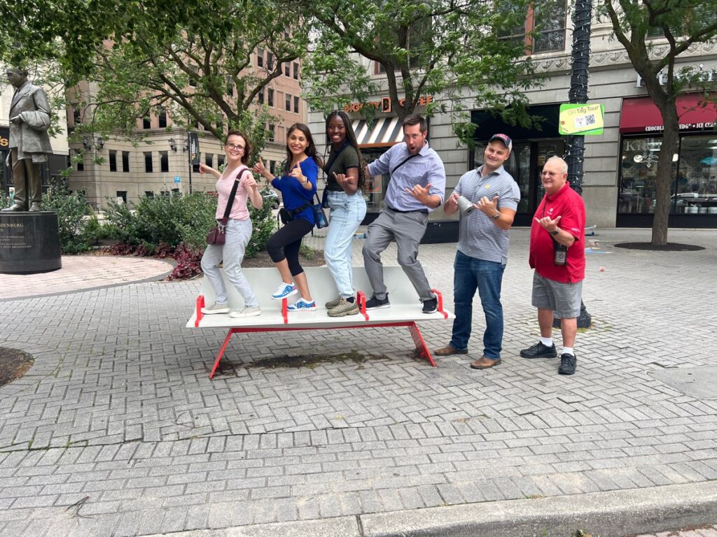 A group of team members standing in a fun pose on a public seesaw during a Team-opoly scavenger hunt team building event in an urban setting.