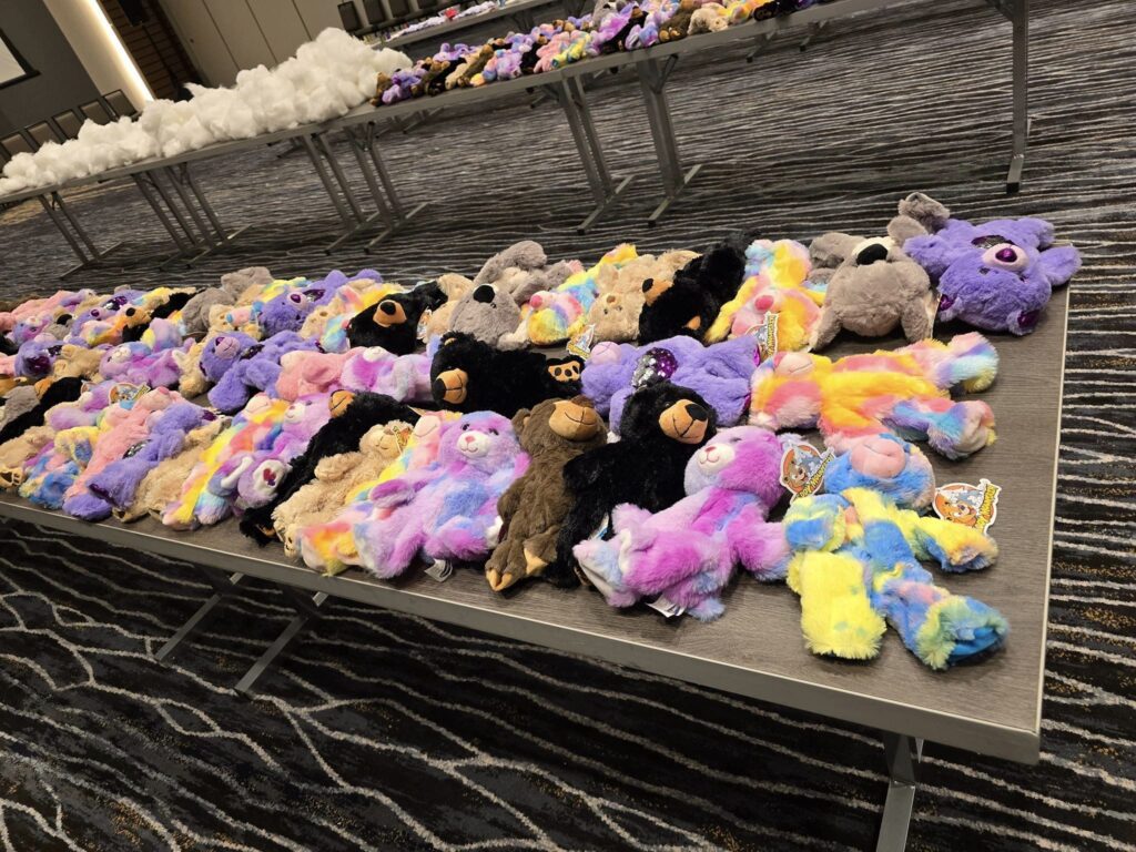 Table filled with colorful stuffed teddy bears laid out during the Team Teddy Bear Rescue activity at a corporate charitable team building event.