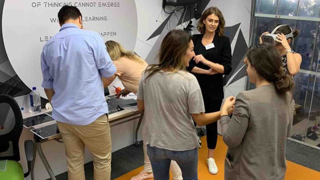 Participants engaging in a collaborative VR challenge at The Infinite Loop team building event, with one member wearing a VR headset while others provide input and work together.