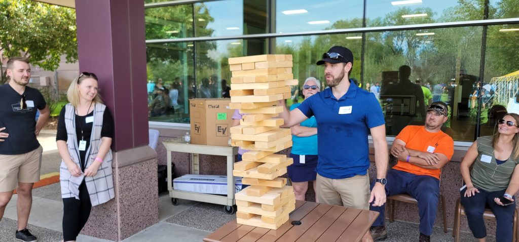 The image shows participants engaging in a giant outdoor Jenga game, a popular activity in the 