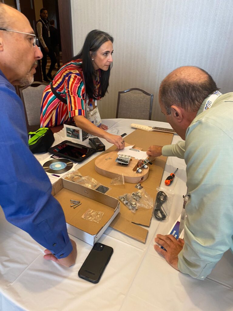 Team members discuss and organize guitar parts during the Charity Guitar Build team building event, preparing to assemble instruments for donation.