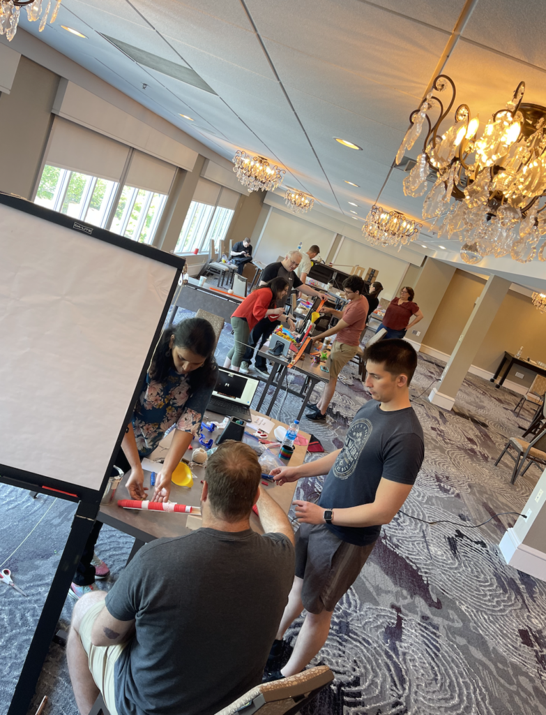 Teams working together in a spacious room, building creative contraptions during the Domino Effect team building event.