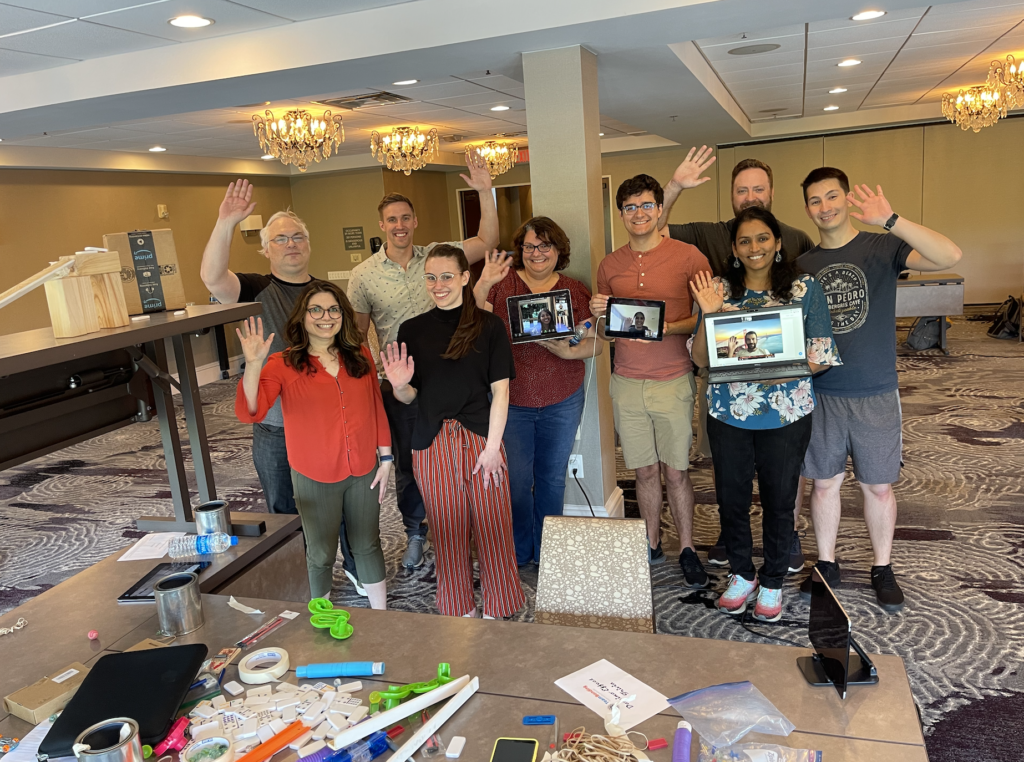 Group of participants proudly waving after completing their Domino Effect team building activity, surrounded by creative contraption materials.