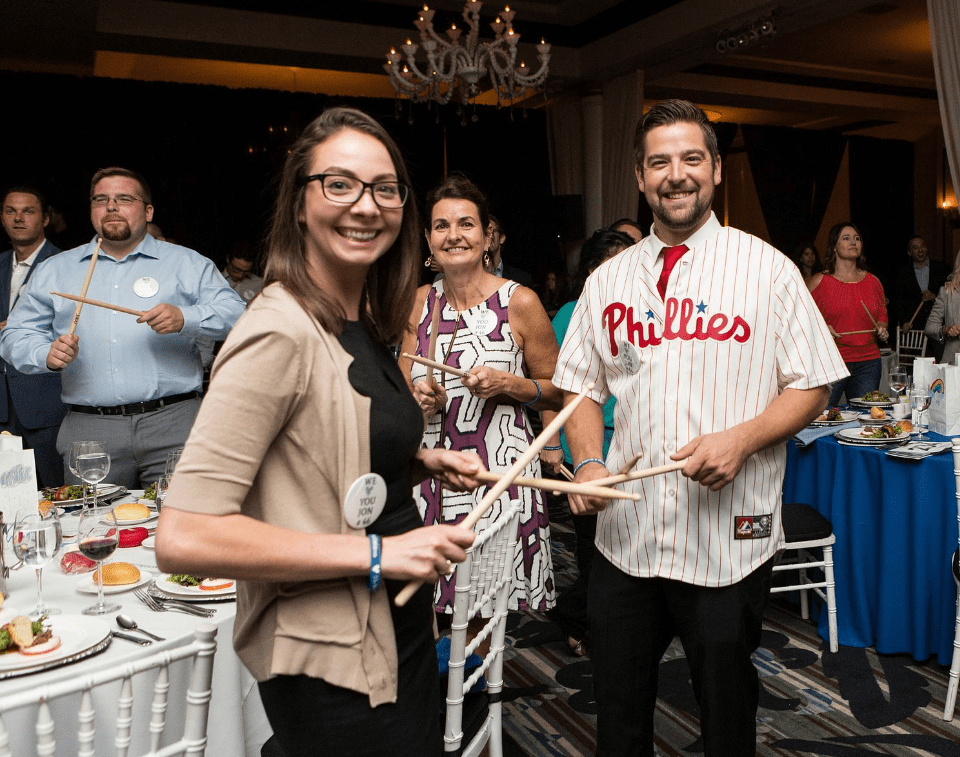 Participants in the Drumming Up A Team event enthusiastically engage in a percussion activity, fostering unity and teamwork while creating an upbeat atmosphere of collaboration and celebration.