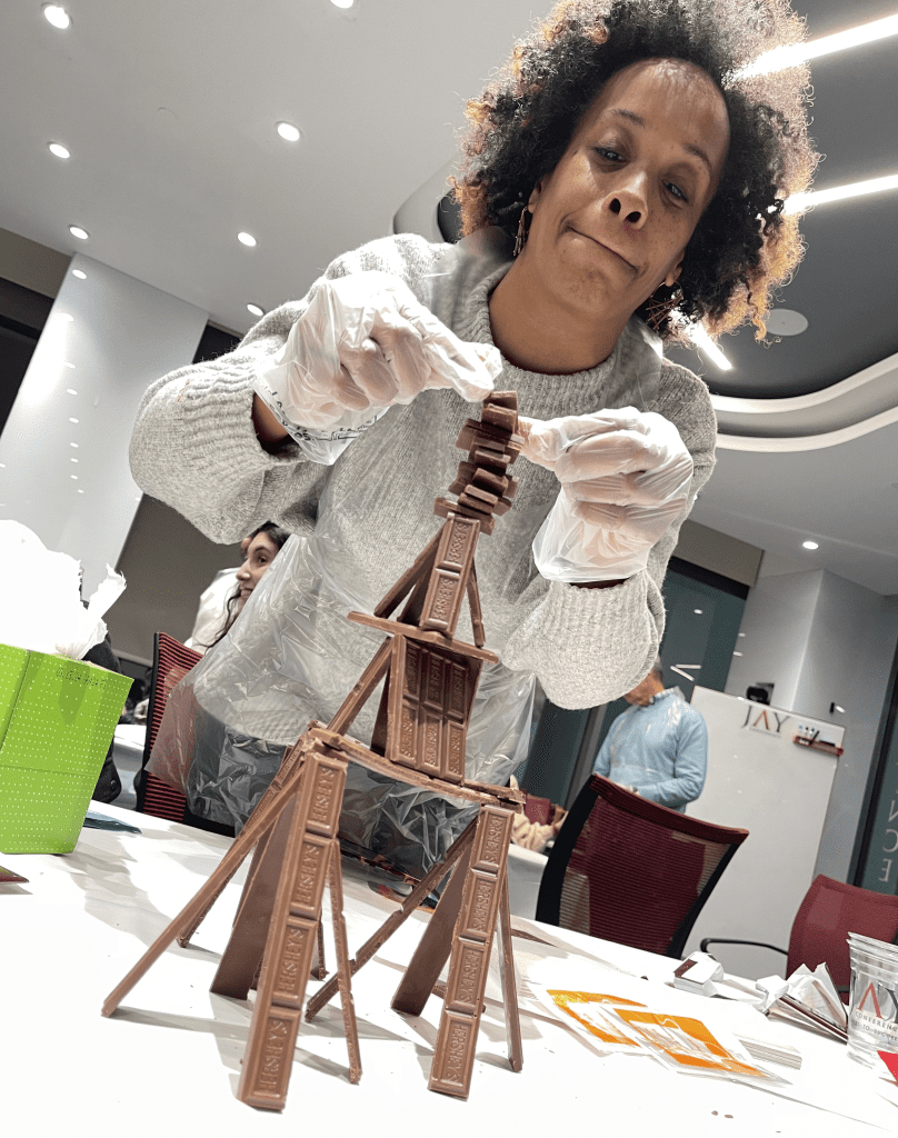 A participant in the Chocolate Challenge team building event carefully stacks chocolate bars to create a stable structure, focusing on precision and creativity.