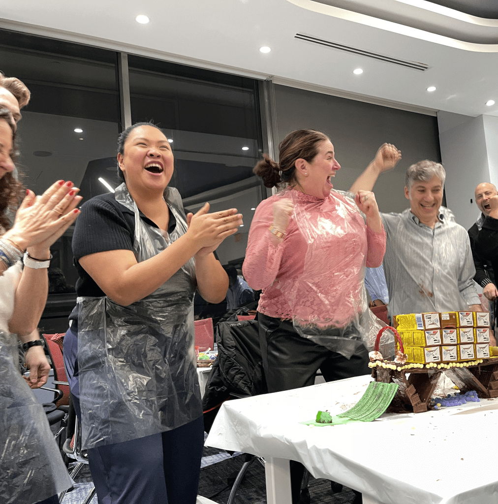 Team members celebrate their success in the Chocolate Challenge team building event, excitedly clapping after constructing their chocolate bridge.