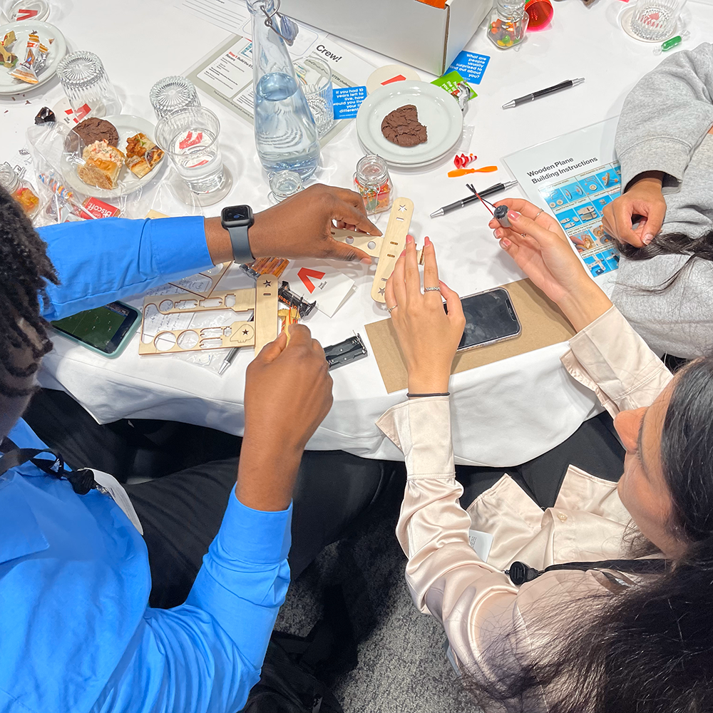 Participants working together at a table, assembling parts of a miniature airplane from a STEM kit during the STEM Speedway team building activity, focusing on teamwork, precision, and hands-on learning.