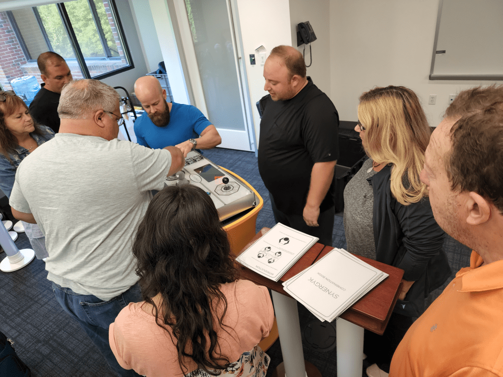 Team members collaborating around a Team Synergy console, discussing strategies and solving interactive challenges during a team building event.