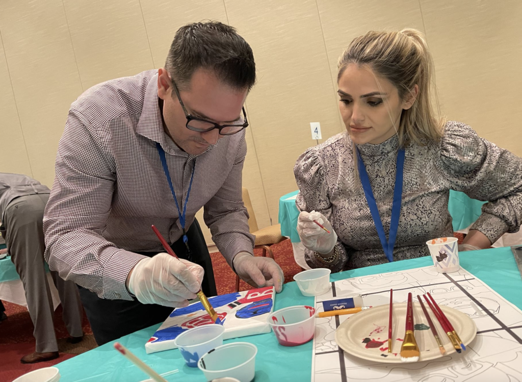 Two participants collaborate on painting a section of a mural during The Big Picture team building event, focusing on precision and teamwork to contribute to the larger artwork.